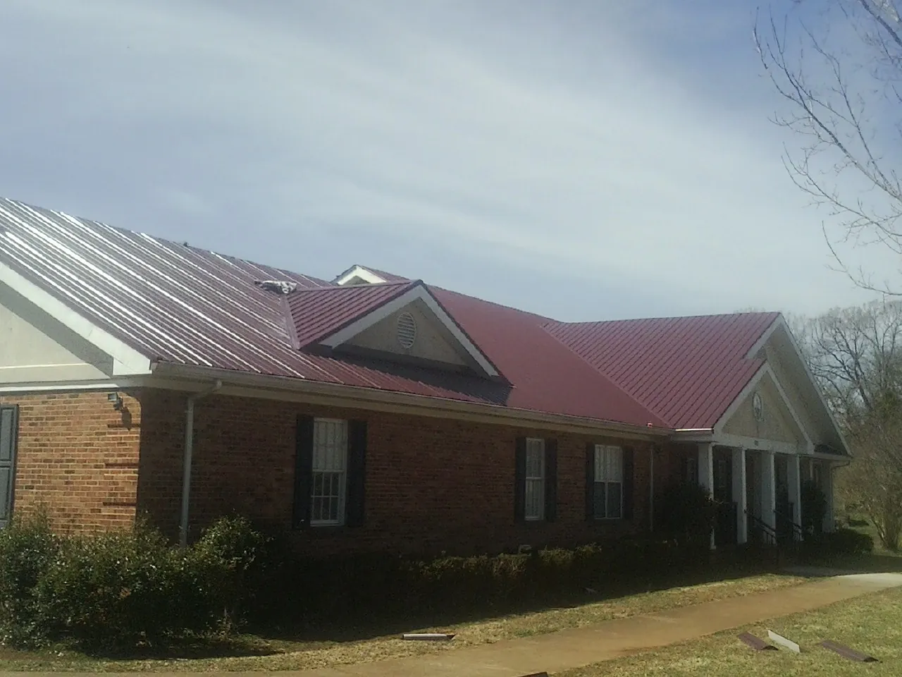 Red metal roof with gabled entries on a long brick building, from a Hail Damage Roof Repair job in South Haven