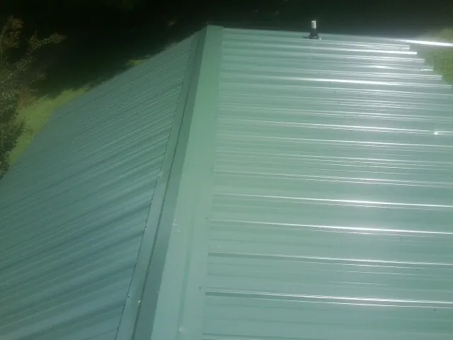 New green metal panels meeting at the ridge of a roof — Flat Roof Repair work by our crew in South Haven