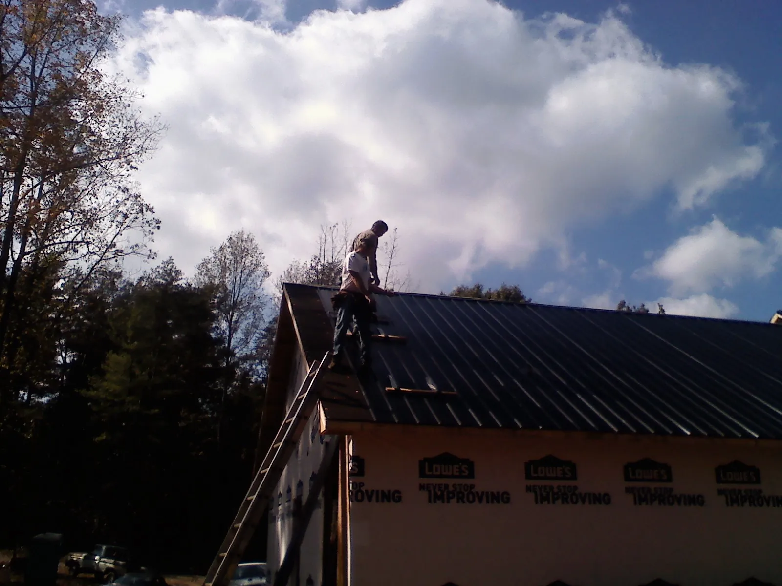 Roofer fastening dark metal panels high against a cloudy sky, from a Roof Inspection job in South Haven